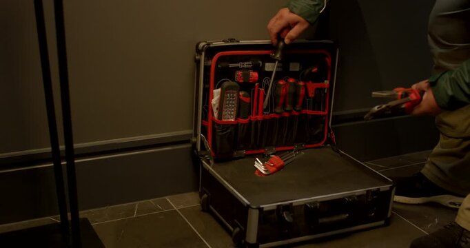 Close up view of a person wearing a green jacket opening a professional tool case on a dark tiled floor