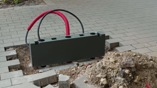 Public walkway compromised by uncovered electrical conduit and uneven paving creating safety dangers