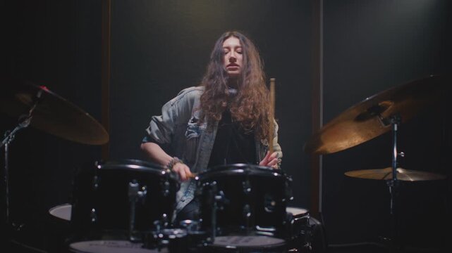 Young female drummer passionately playing a drum kit in a professional rehearsal studio, energetically striking cymbals and drums with drumsticks. Hair flying. Rock Feminist style. Woman power.