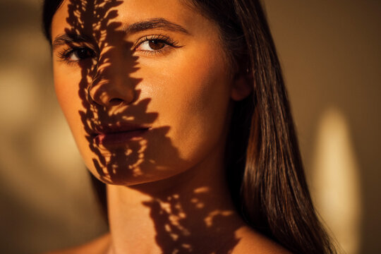 Young woman with long dark hair, illuminated by soft light, showcasing intricate shadows on her face, creating a captivating and artistic visual experience