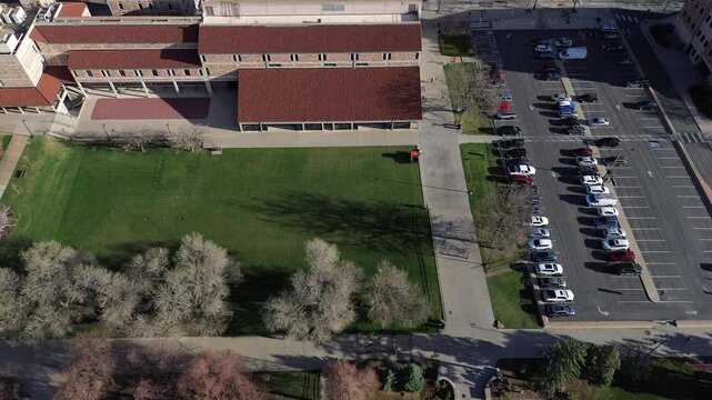 Lawn and building alignment east of Broadway with large academic building, walkways, parking corridors linking to residential blocks, foothill edge streets. Tan stone walls, red roofs, Boulder, CO