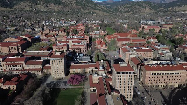 Folsom district overview near adjacent athletic district anchors scene with stadium structures, campus housing, walkways extend toward foothills. Red tile roofing, patterned shadows, Boulder, CO