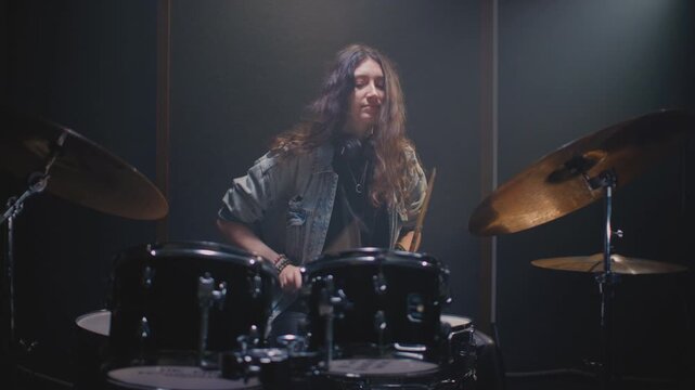 Drummer girl playing drums in music rehearsal studio filled. Rock band music artist learning a drum solo. Young woman with long curly hair, fill or break on drum kit. Female drumming in room