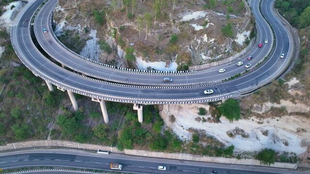Top-down drone shot of curved highway infrastructure in Jammu. 
High-altitude top-down view of a winding S-curve road. 