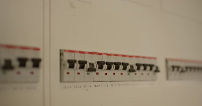 Row of automatic circuit breakers with red switches installed inside a white electrical distribution board