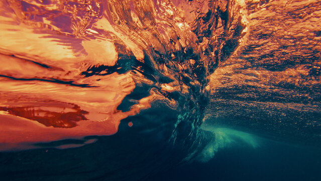 Underwater view of a breaking ocean wave with golden sunset light reflecting through the water surface and dynamic textures.