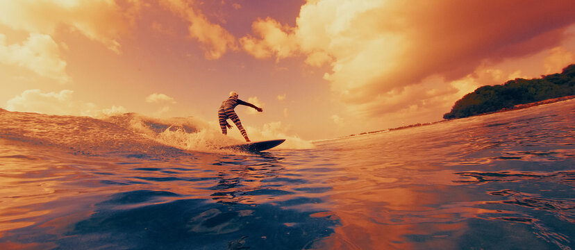 Surfer riding a wave at sunset with warm golden light