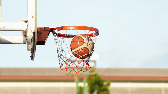 Basketball going through hoop in outdoor court with copy space and bright daylight
