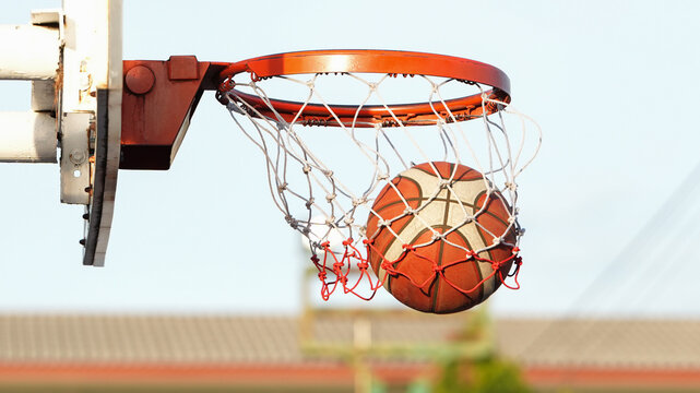 Outdoor basketball hoop with ball entering net, symbolizing score, competition, and success