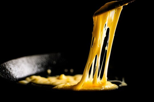 Melted Fontina cheese bubbling and stretching, showcasing its delicious gooey texture in a dark culinary setting