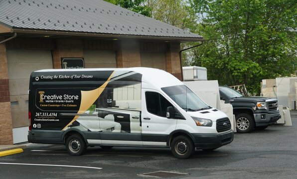 Pennsburg, Pennsylvania, U.S - May 12, 2026 - Creative Stone service van advertising custom countertops parked near stone slabs outside commercial building.