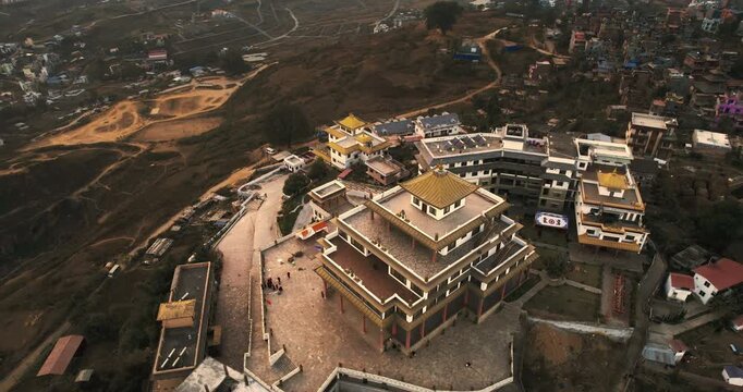 Aerial drone view of the Chovar Gumba monastery complex in Nepal, featuring golden pagoda roofs and white buildings set against the surrounding hills and city outskirts.