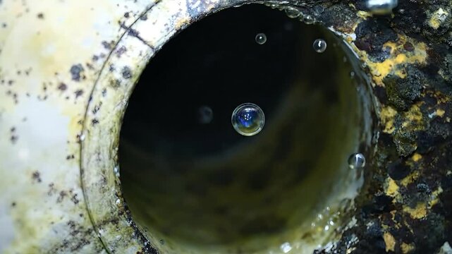 Bubbles float near a rusty, dirty pipe opening, in a macro view.