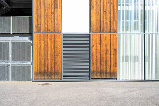 Warm wood panels break the modern facade between glass, metal doors and a pale curtain, while the sidewalk keeps the urban architecture calm