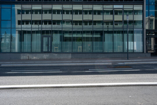 A glass office facade stretches beside the road, where reflection moves across windows and the street sidewalk frames the urban building