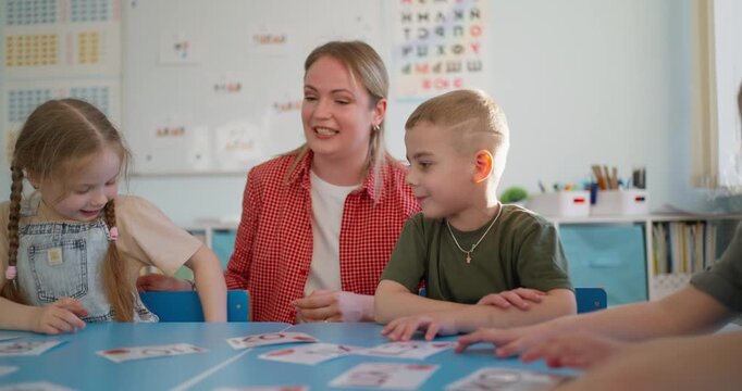 Young children and teacher practice letters with flashcards at a classroom table during a bright, playful early learning lesson