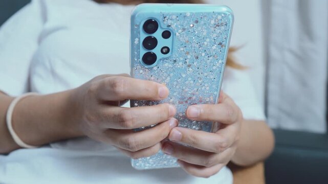 Person holding smartphone with light blue glitter case and multi lens camera, actively using device for browsing, messaging, social apps and everyday mobile connectivity close up