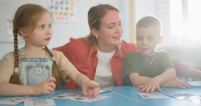 Teacher guiding young children during a playful classroom card activity, encouraging early learning, cooperation, and engagement around a table