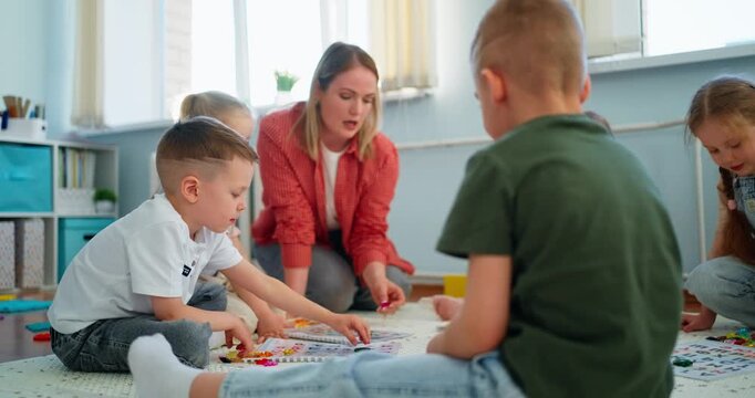 Teacher guiding young children in a bright classroom as they sit on a carpet playing an educational board game with colorful pieces together