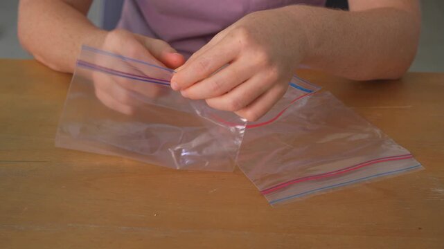 Close up hands opening plastic ziplock bags at table with crisp sound. Woman unsealing resealable packaging creating satisfying noise. ASMR, sensory experience and everyday task concept.