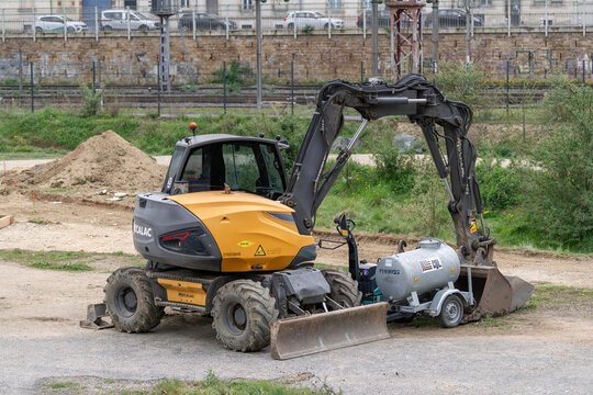 Nancy, France - April 10th 2026 : View on a yellow wheeled excavator Mecalac 15MWR for earthworks on a construction site with vegetation in the background.