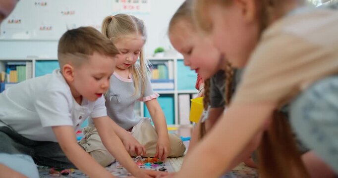 Young children and teacher sitting on classroom floor playing a colorful educational board game during a collaborative preschool learning activity
