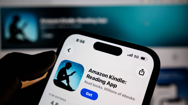 Closeup of a hand holding an iphone displaying the amazon kindle reading app page in the apple app store