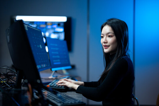 Young female software engineer writing program code on multiple desktop screens in a modern office.
