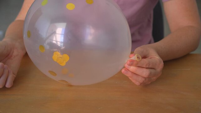 Woman sitting at table deflating inflated balloon with distinctive sound. Close up hands releasing air creating squeaky noise. ASMR, sensory experience, sound design and playful concept.