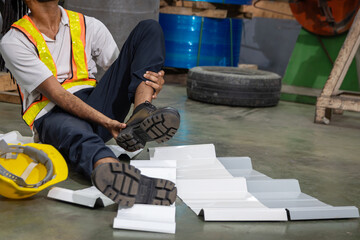 An industrial male engineer injured his leg in an accident at an industrial worksite, lying on floor at manufacturing factory. An injured man worker at workplace feeling in pain and need help.