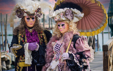 Obraz premium Two splendid masks with umbrellas disembark from the gondola in the lagoon in Venice