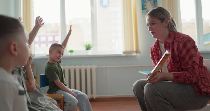 Female teacher kneeling with a book while speaking to young students in a bright classroom, creating a warm learning and counseling atmosphere