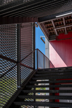 A metal stairway rises beneath a colorful urban facade, where shadow, railing, structure, exterior light, and architecture frame the passage