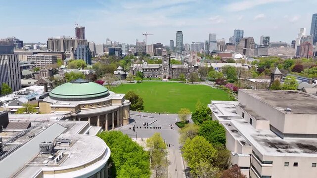 Aerial view flying forward over King's College Circle toward the historic romanesque revival facade of University College in Toronto
