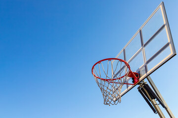 Naklejka premium Low angle shot of basketball hoop on sunny day outside at basketball court in city park. Basketball basket with white backboard against blue sky. Achievement, sports concept