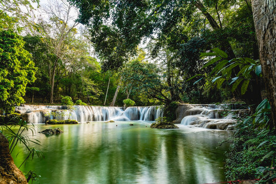 Beautiful Chet Sao Noi or Seven Little Girls Waterfall in Saraburi Thailand. Scenic wide cascade flowing into a serene emerald pool surrounded by lush green tropical forest trees.