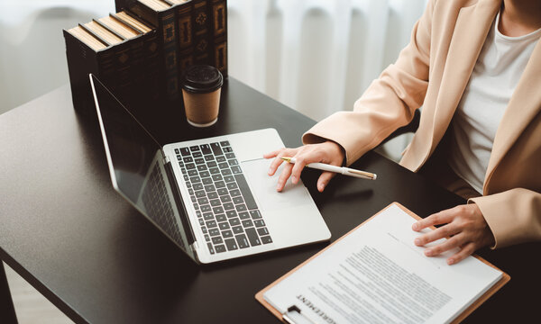 Businesswoman working on laptop and reviewing documents in office, managing paperwork, agreements, and legal contracts at her desk
