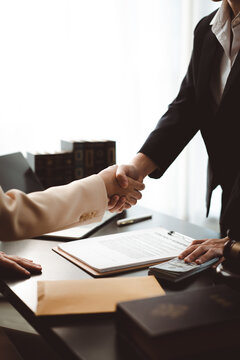 Two professionals shake hands over contracts, cash and legal books on a desk, suggesting a secretive or corrupt business deal, bribery or illicit financial agreement