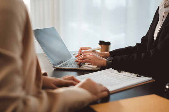 Businesswoman typing on laptop during a corporate meeting, discussing a contract document with a client, focusing on agreement terms and professional collaboration