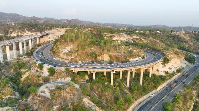 High-angle view of sharp S-curve road and structural pillars at golden hour sunset.
Dramatic high-angle aerial overlooking a tight hairpin turn on a vital Indian highway.