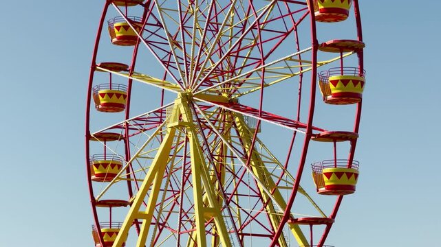 A bright red and yellow Ferris wheel towers into a clear blue sky. This cheerful sight brings back happy memories of childhood fun, excitement, and carefree summer days.