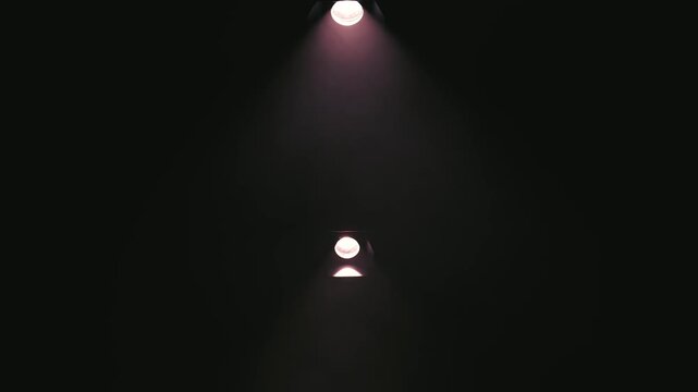 Symmetrical vertical shot of two magenta spotlights fixed on a dark stage ceiling. Smooth downward camera movement reveals the rich purple lighting beams cutting through the darkness