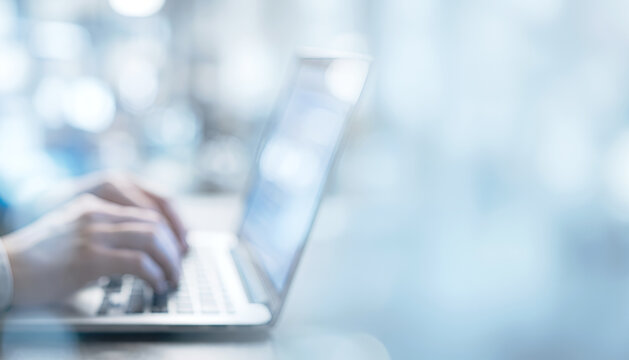 A close-up of hands typing on a laptop keyboard, showcasing a modern and minimalistic workspace setting with a blurred background.