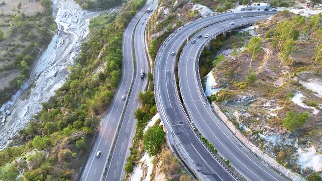 Aerial view of rapid infrastructure development in rural India. High-altitude aerial establishing shot of a winding transportation route snaking through a massive, dry riverbed.