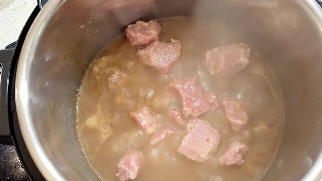 Close-up of meat chunks cooking in a savory broth inside a pot.