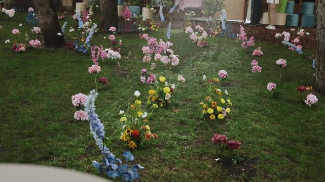 At wedding party decor raining on luxury ground flowers in green grass lawn close up in forest 4K. Elegant outdoor wedding ceremony floral installation during rainy weather, wet blooming plants and