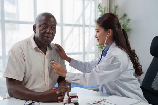 Female doctor providing medical examination for a senior Black man, using stethoscope to check a patient's heartbeat in clinic for health and wellness