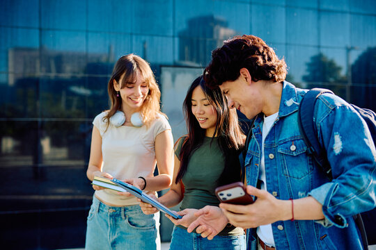 Three diverse students sharing information and smiling while standing outside a university building