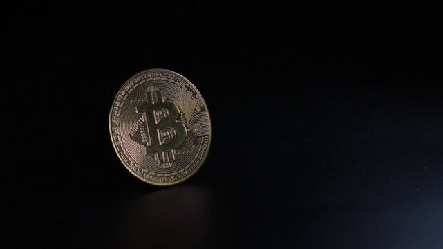 Cryptocurrency bitcoin coin standing vertically on a reflective dark surface in a studio environment while moving lights create glowing reflections and metallic highlights, representing digital financ