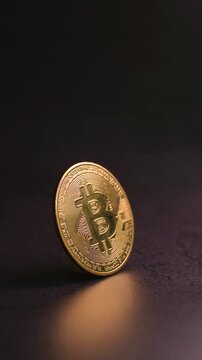 Vertical video of a golden bitcoin cryptocurrency coin standing on a dark granite surface in a studio setting while the camera slowly pushes in, representing blockchain technology, digital finance, cr